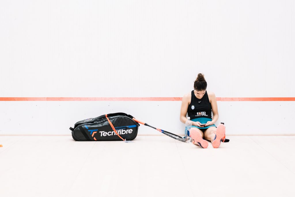 PSA Player checks her phone sitting on the court floor